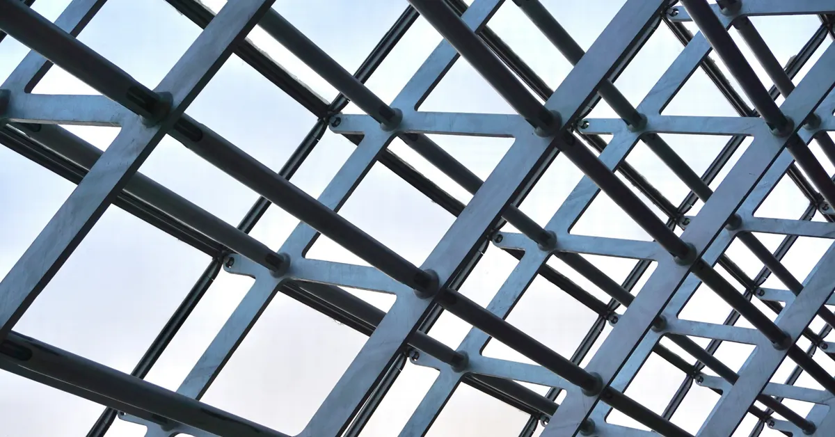 Steel lattice roof structure seen from below against a pale sky